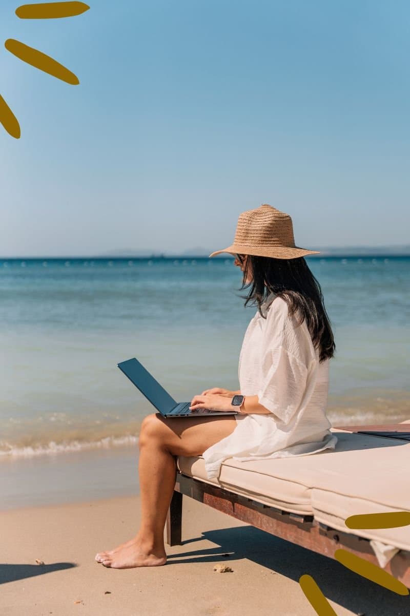 Frau mit Sonnenhut arbeitet am Laptop am Strand
